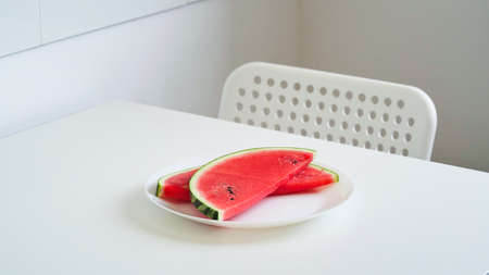 Close-up slices of fresh ripe red watermelon on a plate with a knife on the table on a white background, half of a watermelon. Ripe juicy summer berries, melon season. Macrophotoの写真素材