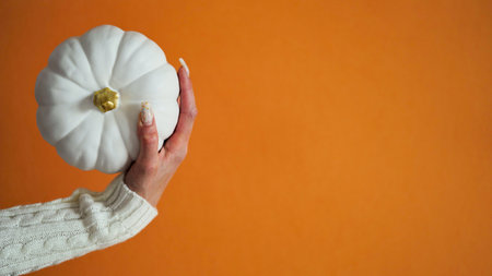 Close-up woman hands white sweater holding figure ceramic pumpkin orange background,copy space.Decor concept Happy Halloween celebration.Thanksgiving,autumn symbol.Beautiful banner.の写真素材