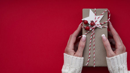 Woman hands white sweater hold Christmas New Year gift box on red background,top view,flat lay,copy...