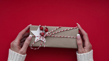 Woman hands white sweater hold Christmas New Year gift box on red background,top view,flat lay,copy space. Christmas holidays celebration concept,gifts for family,friends.Winter banner,space for textの写真素材