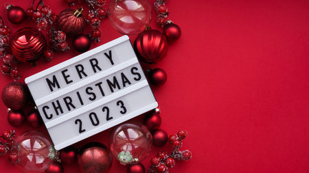 Marry christmas banner concept. White board with the text Marry Christmas 2023 among Christmas red decor, balls and berries on a red background, top view, flat lay, copy spaceの写真素材