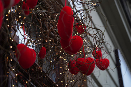 Close-up of red velvet hearts on willow branches among garland of lanterns,festive decor for Valentine's Day.Beautifully decorated shop window in the city.Cityscape, hearts in snow.の写真素材