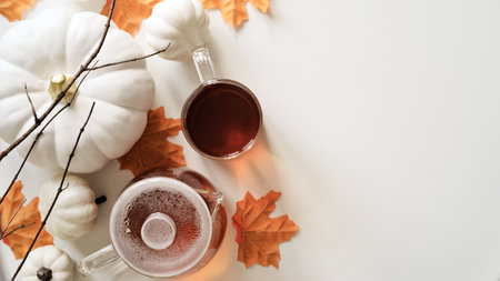 Close-up of cup of tea, glass teapot, pumpkins, orange maple leaves, twigs and book on white...