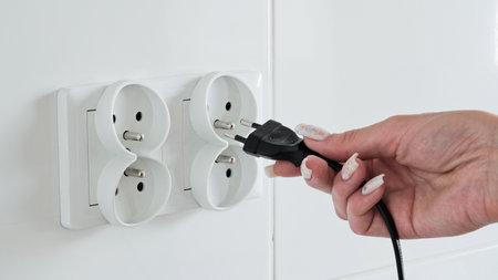 Close-up of a female hand inserting a black electric plug into a double European electrical socket...
