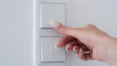 Close-up woman's hand turns off the white wall light switch, copy space, space for text. The concept...
