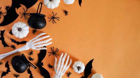 Close-up holiday decor: pumpkins, bats, pots, spider skeleton, autumn leaves and eyes on an orange background, top view, copy space. Halloween celebration concept, decor for All Hallows' Day.の写真素材