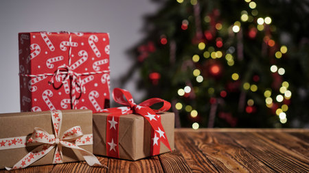 Many gift boxes wrapped in multi-colored paper on a wooden table against the background of a beautiful Christmas tree, copy space. Merry Christmas and Happy New Year greeting conceptの写真素材