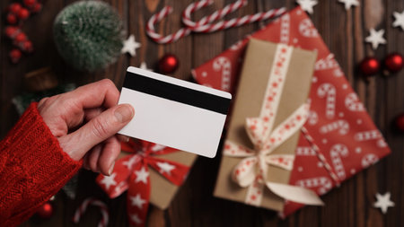 Hands of a woman in a red sweater with a credit card on a background of gift boxes, selective focus, close-up. Christmas and New Year shopping online, payment by credit card. Buying gifts onlineの写真素材