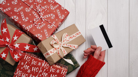 Hands of woman in red sweater holding credit card and gift box on white background close-up,top view,flat lay,copy space.Christmas and New Year online shopping,credit card payment.Buying gifts onlineの写真素材