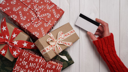 Hands of woman in red sweater holding credit card and gift box on white background close-up,top view,flat lay,copy space.Christmas and New Year online shopping,credit card payment.Buying gifts onlineの写真素材