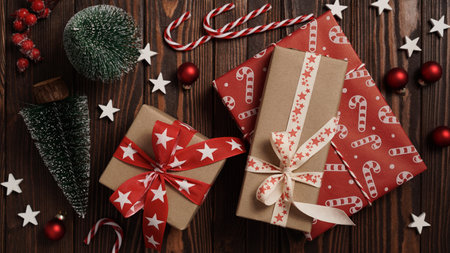 Close-up of Christmas gifts lie on a brown wooden table among holiday decor, fir trees, balls, stars and striped candies, top view, flat lay, copy space. Christmas and New Year banner conceptの写真素材