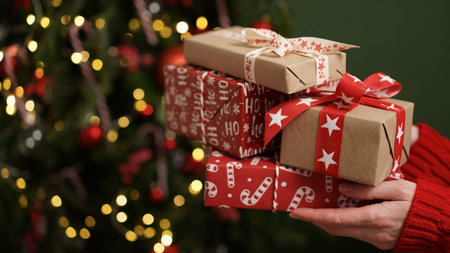 Female hands in red sweater hold Christmas New Year gift box on background of Christmas tree.Giving gifts for holidays.Christmas holidays celebration concept,gifts for family,friends.Winter banner.の写真素材