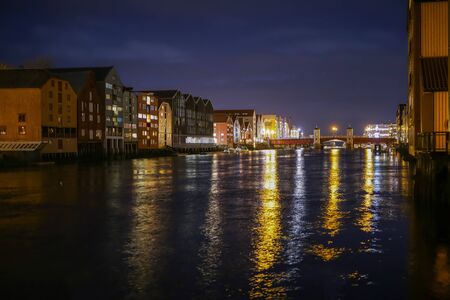 River Nidelva, the bridge Bakke Bru and historical timber buildings along the river in the nighty...