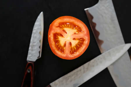 Knives and cutted tomato on the black boardの写真素材