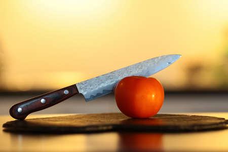 Knives cutting tomato on the wooden board with yellow backgroundの写真素材
