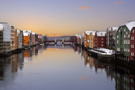 View of the river Nidelva in the snowy Trondheim, the brudge Bakkebru and historical timber buildings along the river reflected in the waterの写真素材