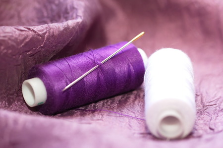 Needle and spools of thread on color textileの写真素材