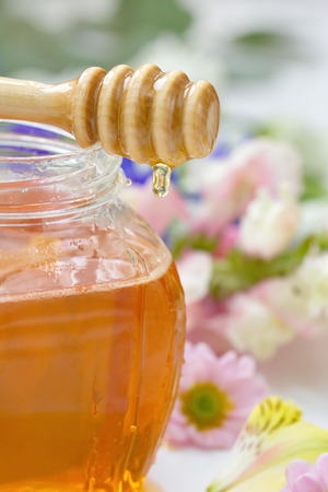 Honey in glass jars with flowers background.の写真素材