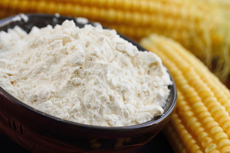 Corn flour in a bowl and corn cob on the table
