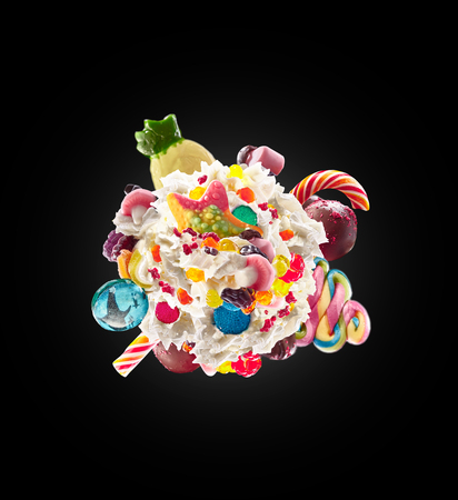 Milk shake with sweets and whipped cream, round form top view. Crazy freakshake food trend. Top view of whipped cream, full of berry and jelly sweets, chocolate candy. Colored whipped cream concept. Monster shake, freak shake concept isolatedの写真素材