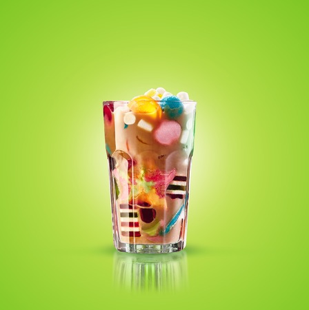 Monster shake, freak caramel shake isolated. Colourful, festive milk shake cocktail with sweets, jelly. Colored caramel milkshake array of different childs sweets and treats in glass on green background. Sweet candy milkshake. Crazy freakshake food trend.の写真素材