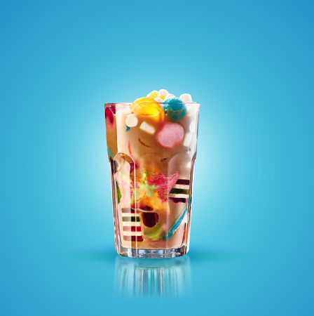 Monster shake, freak caramel shake isolated. Colourful, festive milk shake cocktail with sweets, jelly. Colored caramel milkshake array of different childs sweets and treats in glass on blue background. Sweet candy milkshake. Crazy freakshake food trend.の写真素材