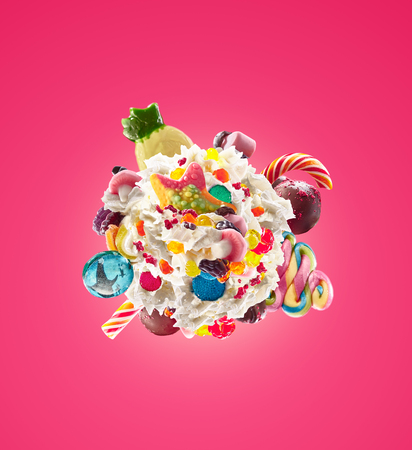 Milk shake with sweets and whipped cream, round form top view. Crazy freakshake food trend. Top view of whipped cream, full of berry and jelly sweets, chocolate candy. Colored whipped cream concept. Monster shake, freak shake concept isolatedの写真素材