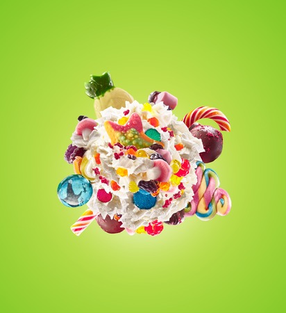 Milk shake with sweets and whipped cream, round form top view. Crazy freakshake food trend. Top view of whipped cream, full of berry and jelly sweets, chocolate candy. Colored whipped cream concept. Monster shake, freak shake concept isolatedの写真素材
