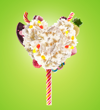Sweet Lolipop in Heart form of whipped cream with sweets, jellies, heart front view. Crazy freakshake food trend. Front view of whipped heart of cream lolly, full of berry and jelly sweets, chocolate candy. Colored whipped heart form cream concept on color backgroundの写真素材