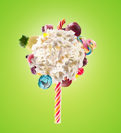 Whipped chantilly cream lolipop concept. Round whipped milk shake cream like lollipop with candy, sweets and candy on border, isolated on bright background. Cream swirl lolly with childs colorful treats, sweet lolipops concept.の写真素材