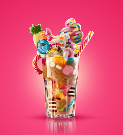 Monster shake, freak caramel shake isolated. Colourful, festive milk shake cocktail with sweets, jelly. Colored caramel milkshake array of different childs sweets and treats in glass on white background. Sweet candy milkshake. Crazy freakshake food trend.の写真素材