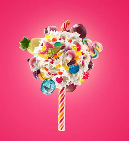 Whipped chantilly cream lolipop concept. Round whipped milk shake cream like lollipop with candy, sweets and candy on border, isolated on bright background. Cream swirl lolly with childs colorful treats, sweet lolipops concept.の写真素材