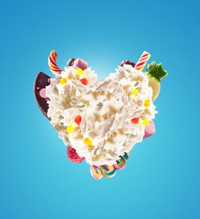 Heart form from whipped cream with sweets, jellies, heart front view. Crazy freakshake food trend. Front view of whipped heart of cream, full of berry and jelly sweets, chocolate candy. Colored whipped heart form cream concept.の写真素材