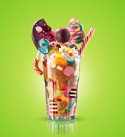 Monster shake, freak caramel shake isolated. Colourful, festive milk shake cocktail with sweets, jelly. Colored caramel milkshake array of different childs sweets and treats in glass on white background. Sweet candy milkshake. Crazy freakshake food trend.の写真素材