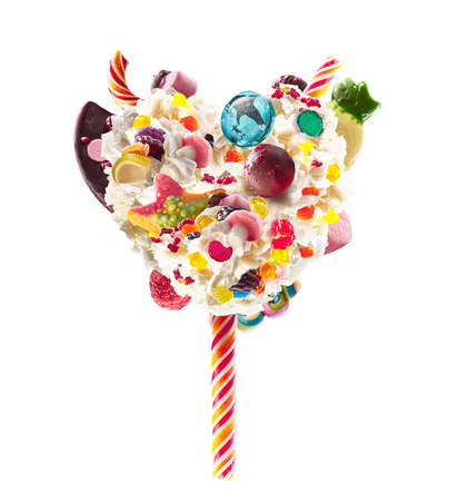 Sweet Lolipop in Heart form of whipped cream with sweets, jellies, heart front view. Crazy freakshake food trend. Front view of whipped heart of cream lolly, full of berry and jelly sweets, chocolate candy. Colored whipped heart form cream concept.の写真素材