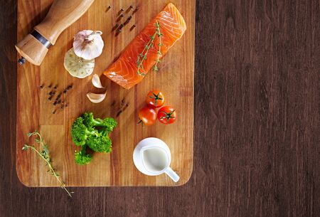 Set of Healthy anticancer food on wooden table. Red salmon fish, broccoli, garlic, milk, pepper and tomatoes scattered around a table. Healthy meal concept, top viewの写真素材