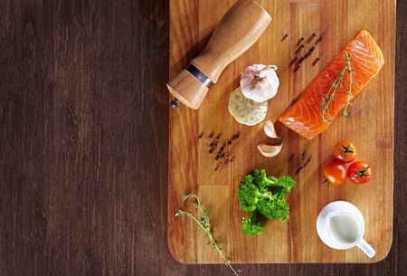 Set of Healthy anticancer food on wooden table. Red salmon fish, broccoli, garlic, milk, pepper and tomatoes scattered around a table. Healthy meal concept, top viewの写真素材