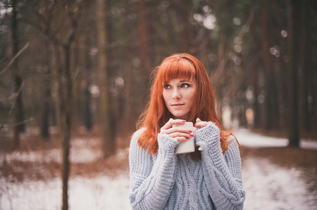 Hipster. Photo redheaded girl with a cup in his hand. Young woman drinking from a cup in the forest.の写真素材