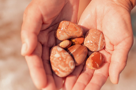 Female caucasian hands holding out rocks and pebbles with more out of focus in the background.の写真素材