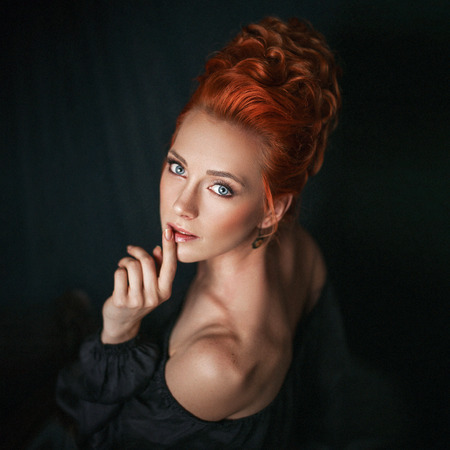 Portrait of redhead woman with blue eyes wearing black dress on dark background.の写真素材