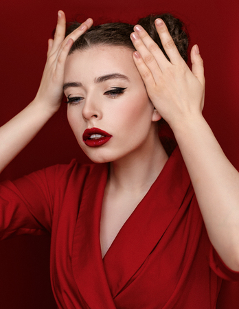 Brunette young woman with red lips wearing red dress on red background. Girl is posing in studio for Valentines day greeting card.の写真素材