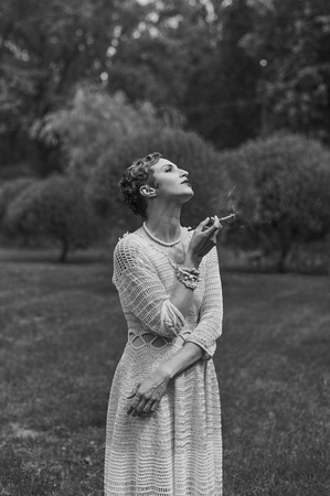 Black and white photography of young smoking woman wearing knitted long dress.  Outdoors image