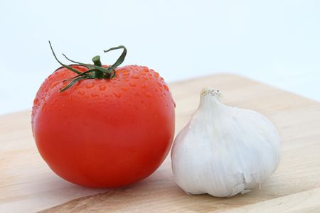A perfect red tomato arranged on a cutting board next to a bulb of garlic.  White background.の写真素材