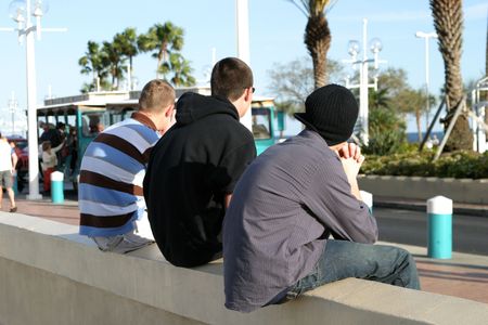 three guys sitting on a wall, watching people pass by on the street.の写真素材