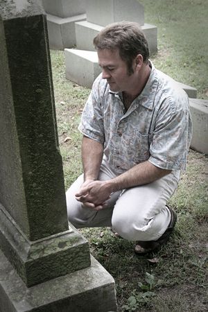 a man in a graveyard with hands folded in reverence - partly desaturatedの写真素材