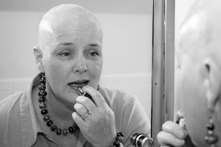 A woman bald due to a health issue, putting on makeup in the mirror.の写真素材