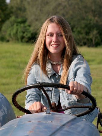 A beautiful farmer's daughter behind the wheel of an antique tractor.の写真素材
