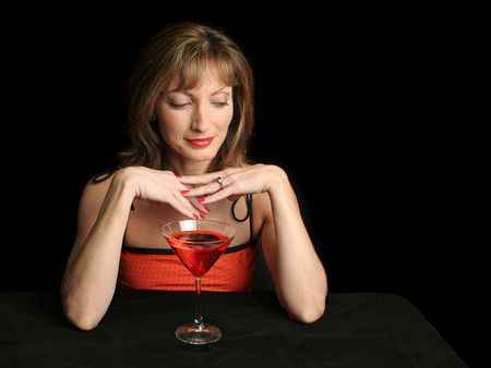 A beautiful woman in red, drinking a cosmopolitan with a suggestive expression.  Photographed against a black background.の写真素材