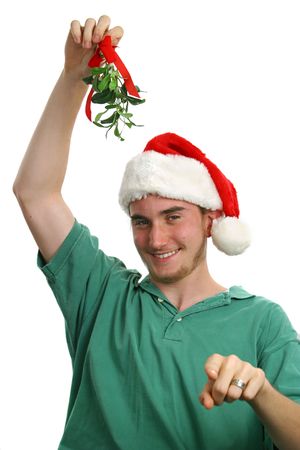 A teen boy in a santa hat holding mistletoe and pointing toward the camera. Isolated.の写真素材
