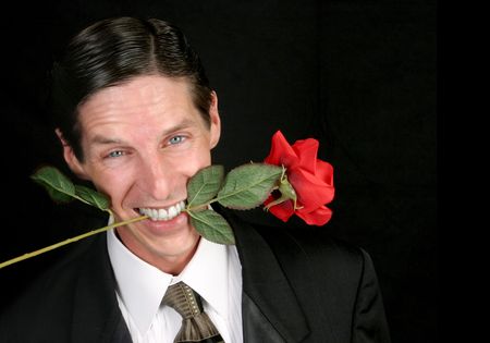 A handsome man with a rose between his teeth - black background.の写真素材